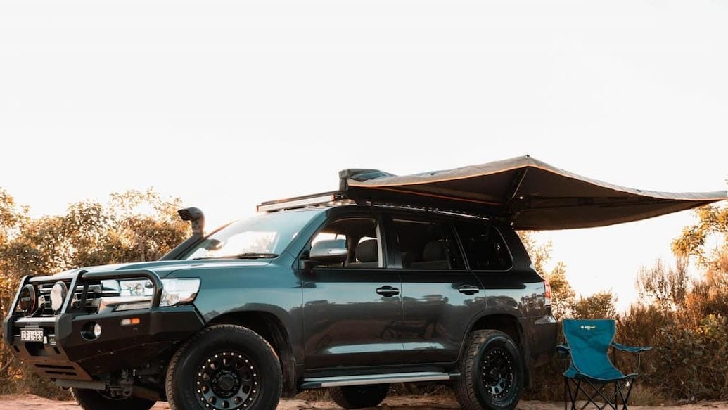 Marco's Toyota Landcruiser on Turo in Sydney, pictured on a camping trip with bushes and a dirt road. The car has a fold out tarp, making it the perfect option for free camping NSW.