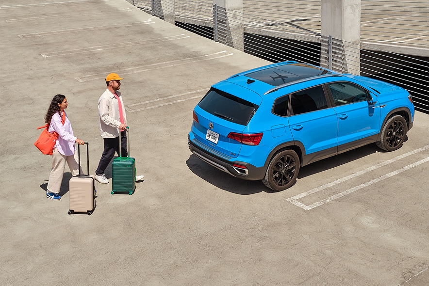 A man and woman prepare to load their blue SUV with their suitcases.
