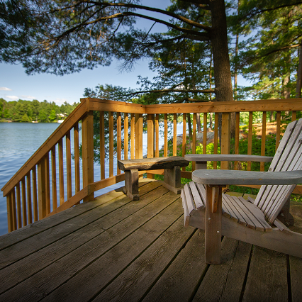 A wooden Muskoka chair on a deck overlooking a lake.