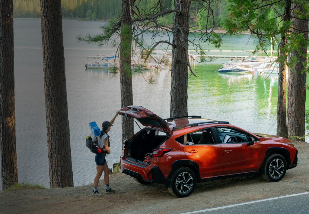 After a hike through the woods, a woman loads her orange SUV with gear.