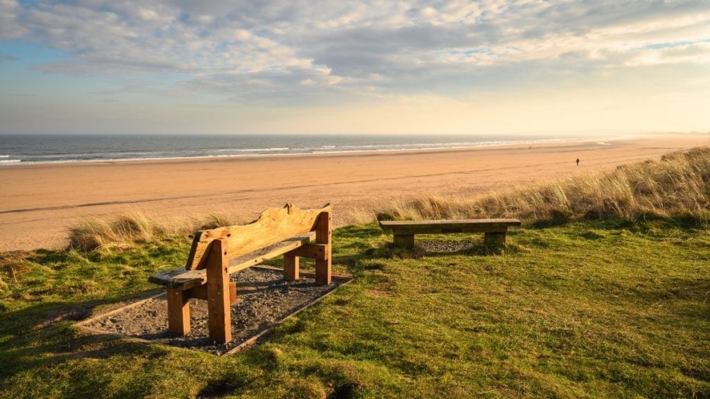 Long sandy beach and grassy dunes at Druridge Bay with a wooden bench facing the sea, Northumberland, England
