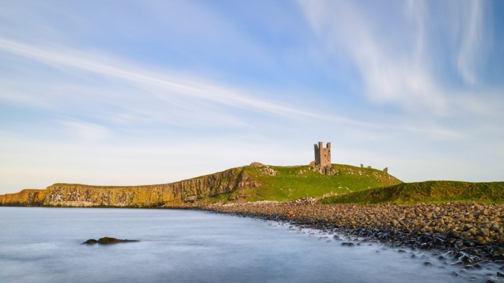 Ruins of Dunstanburgh Castle perched on a grassy headland above the sea, Northumberland, England