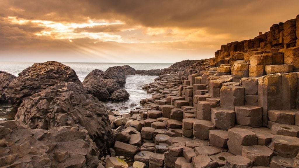 Giant’s Causeway basalt columns rising from the shoreline, with cliffside trail above, County Antrim, Northern Ireland