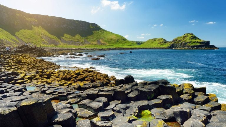 Giant’s Causeway rock formations along the Causeway Coastal Route in Northern Ireland, with hexagonal basalt columns and waves crashing in the background.