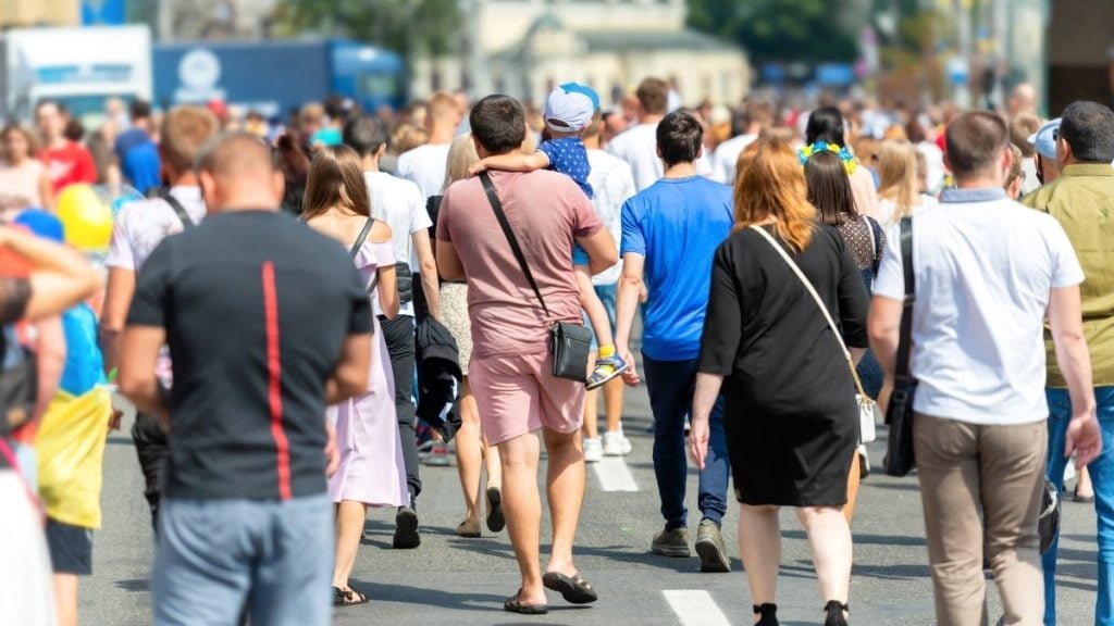 Large crowd of people walking along a busy street.
