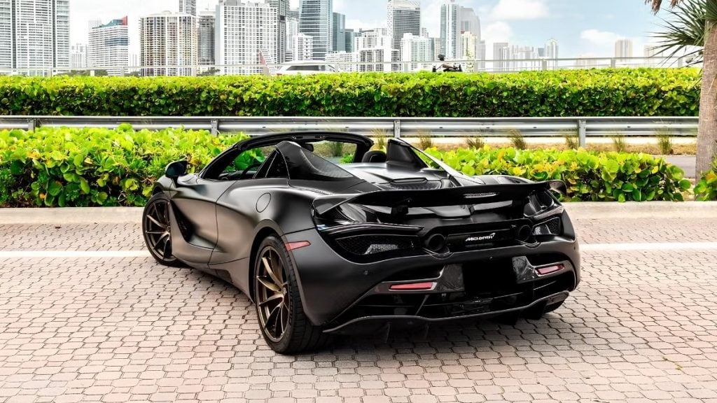 Rear view of a matte black McLaren 720S with bronze wheels, active rear wing, and quad tailpipes parked near the Miami skyline