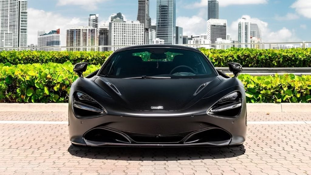 Front view of a matte black McLaren 720S showing its signature eye socket headlights and air intakes against the Miami skyline
