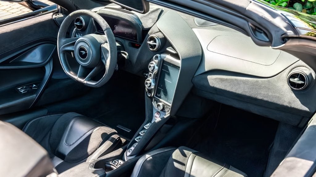 Interior of a McLaren 720S with carbon fiber steering wheel, Alcantara trim, and portrait-oriented touchscreen infotainment display