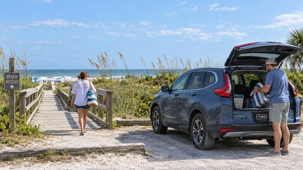 Travelers unloading beach gear from a rental SUV near a coastal boardwalk.